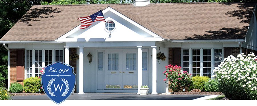 Wenhold Insurance Agency - Office Building with American Flag Blowing in the Wind and Flowers Blooming Around It